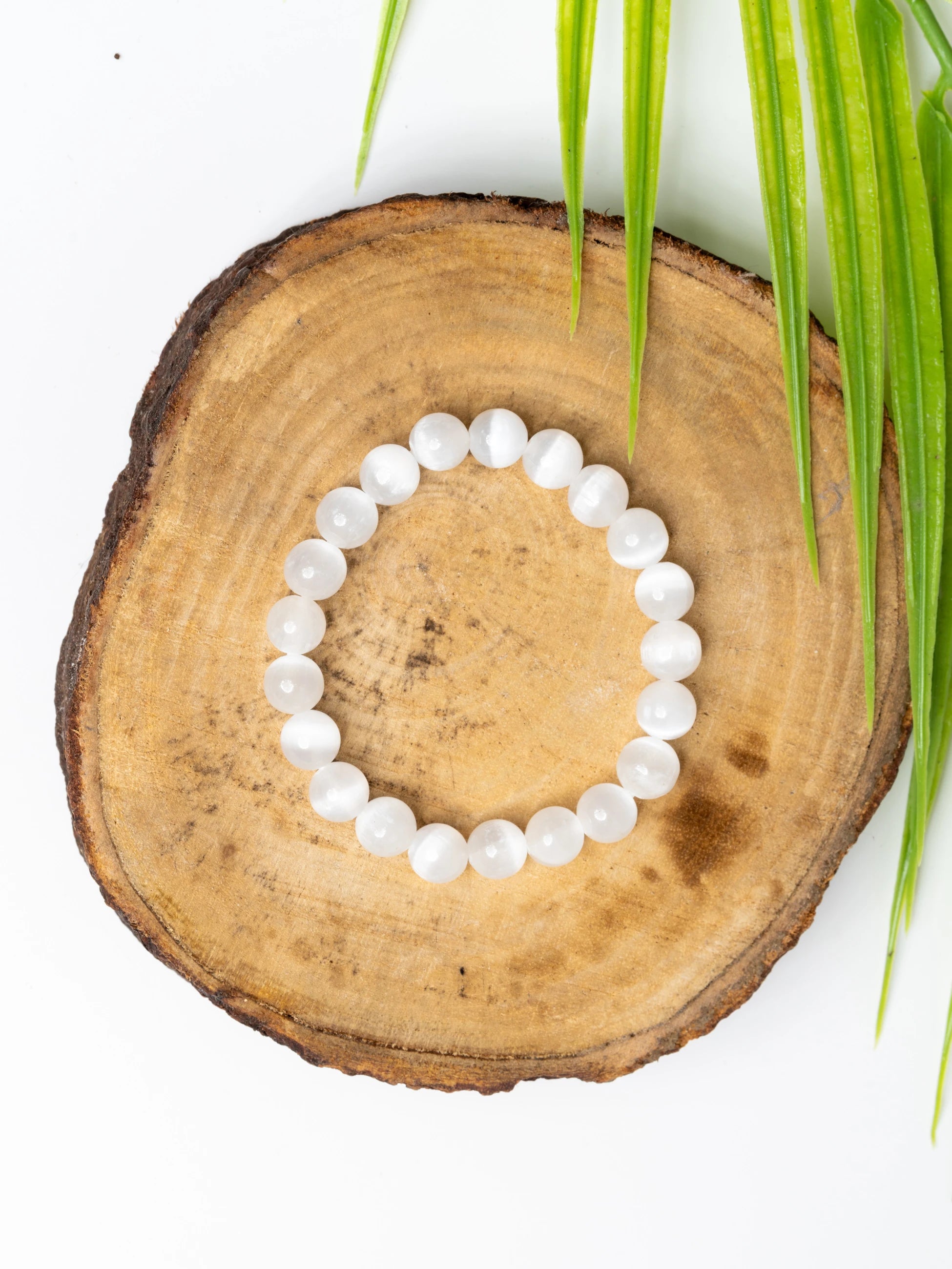 Selenite bracelet made of smooth, polished beads on a wooden surface with green leaves