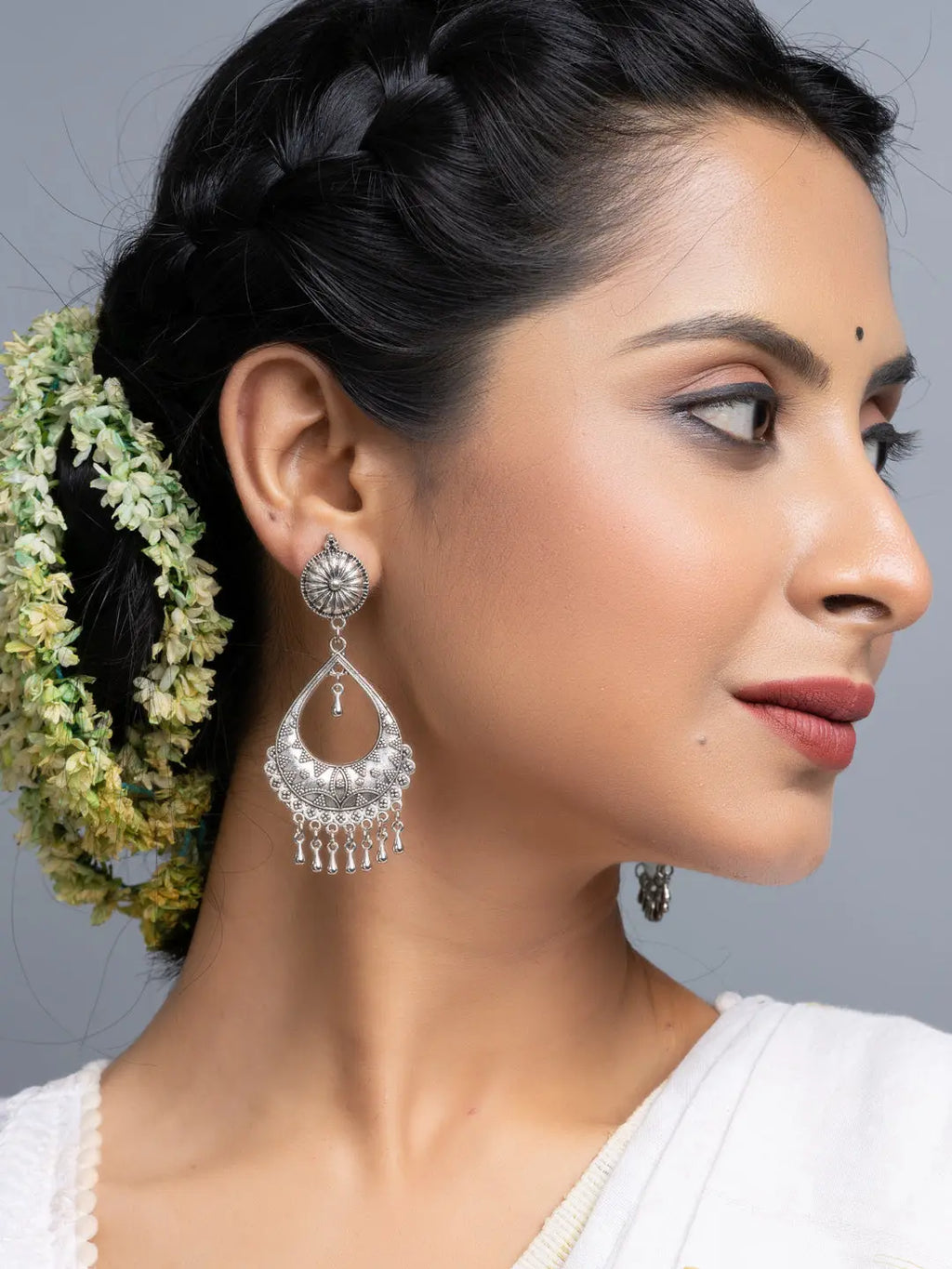 Oxidised silver chandbali earrings worn by woman with braided hair and floral accessory