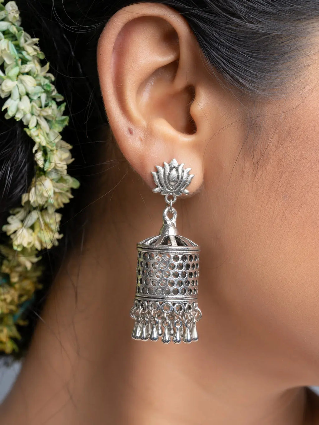 Oxidised silver jhumka earrings worn on ear with intricate design and dangling elements