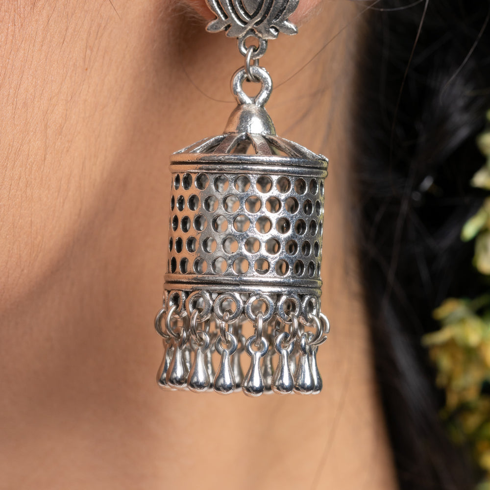 Oxidised silver jhumka earrings with intricate detailing and hanging tassels worn on ear
