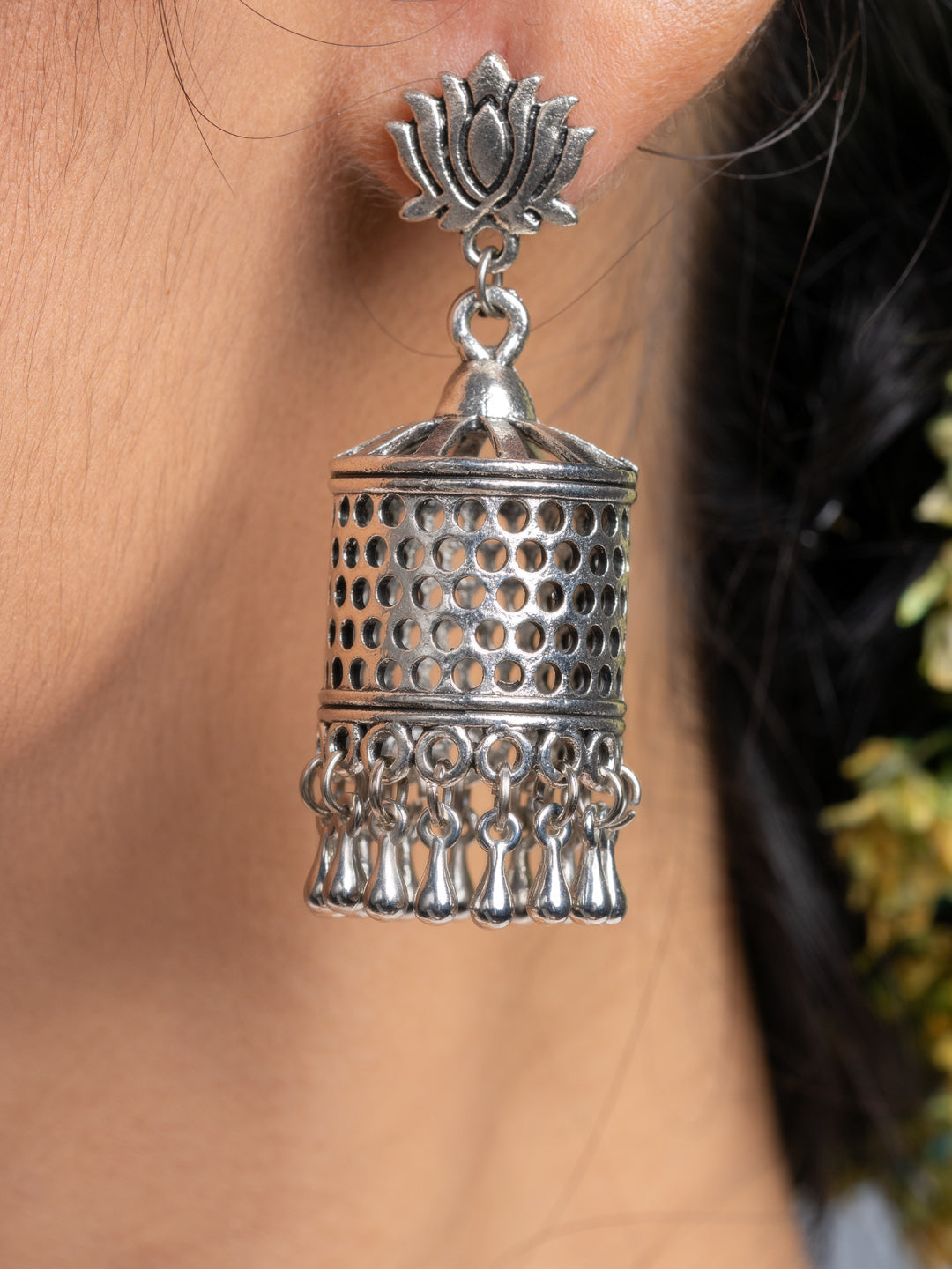 Oxidised silver jhumka earrings with intricate detailing and hanging tassels worn on ear