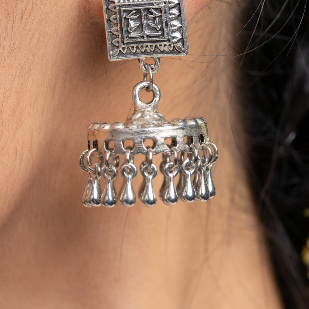 Oxidised silver jhumka earrings with intricate square design and dangling elements worn on ear