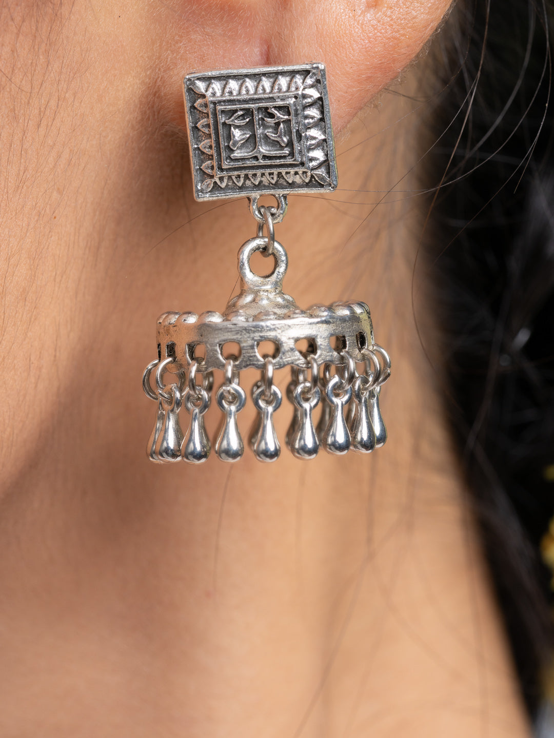 Oxidised silver jhumka earrings with intricate square design and dangling elements worn on ear