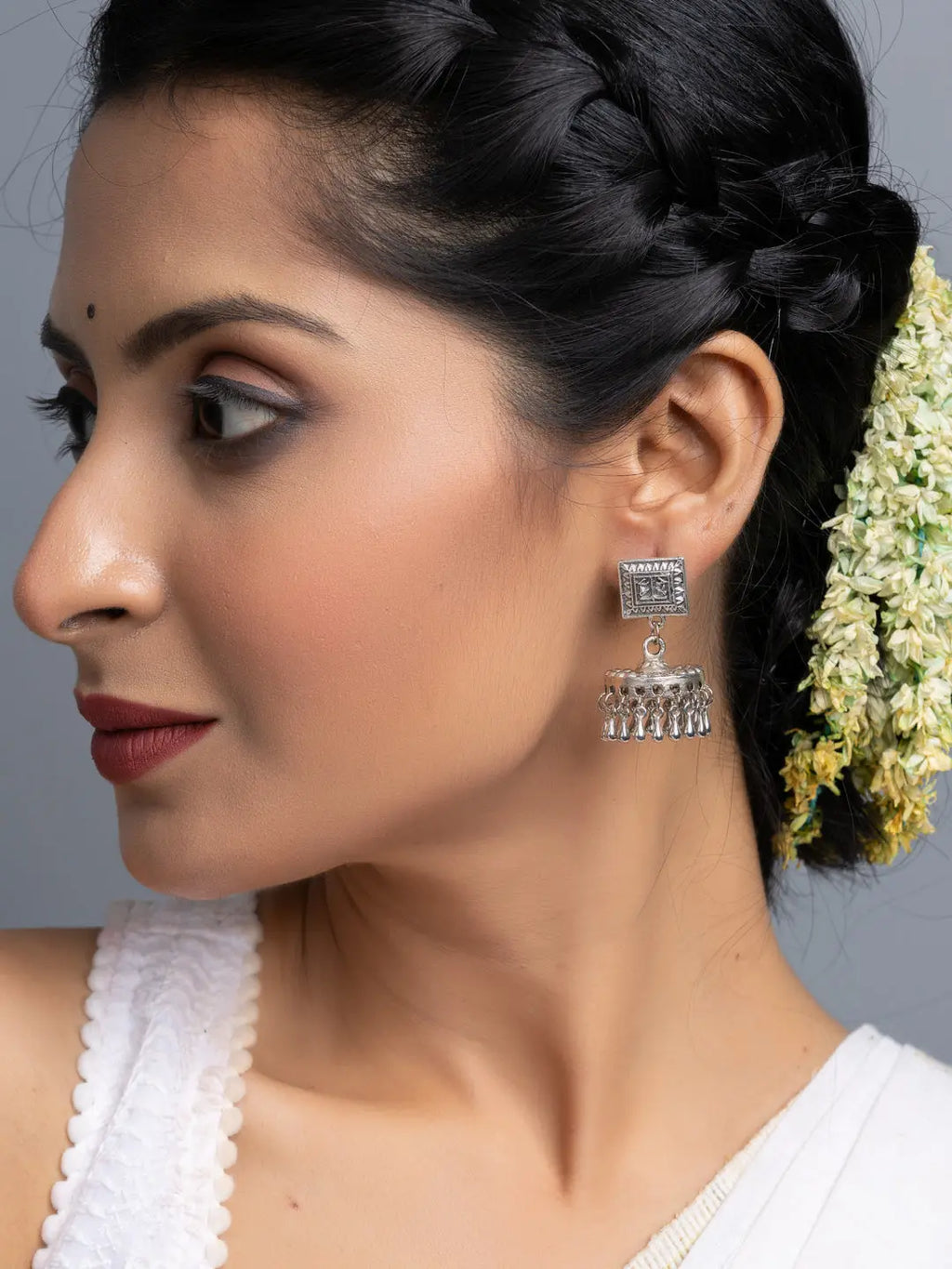 Oxidised silver jhumka earrings worn by woman with braided hair and white floral accessory