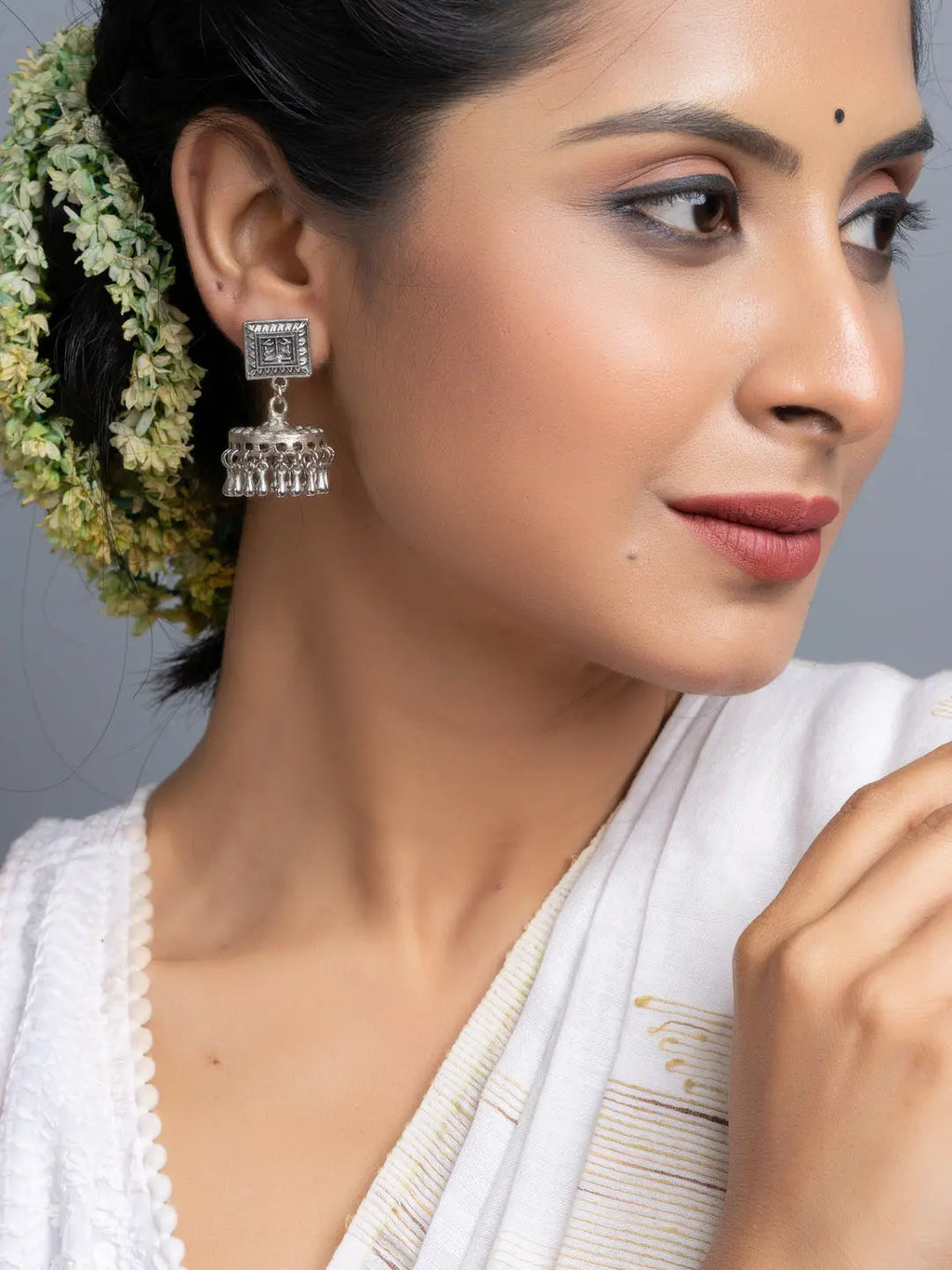 Oxidised silver jhumka earrings worn by woman with traditional white attire and floral hair accessory