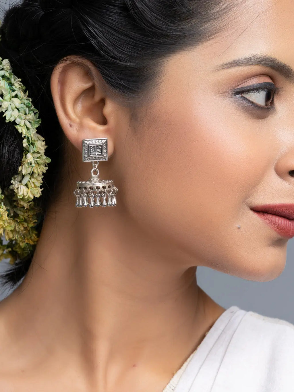 Oxidised silver jhumka earrings worn by woman with traditional hairstyle and white outfit