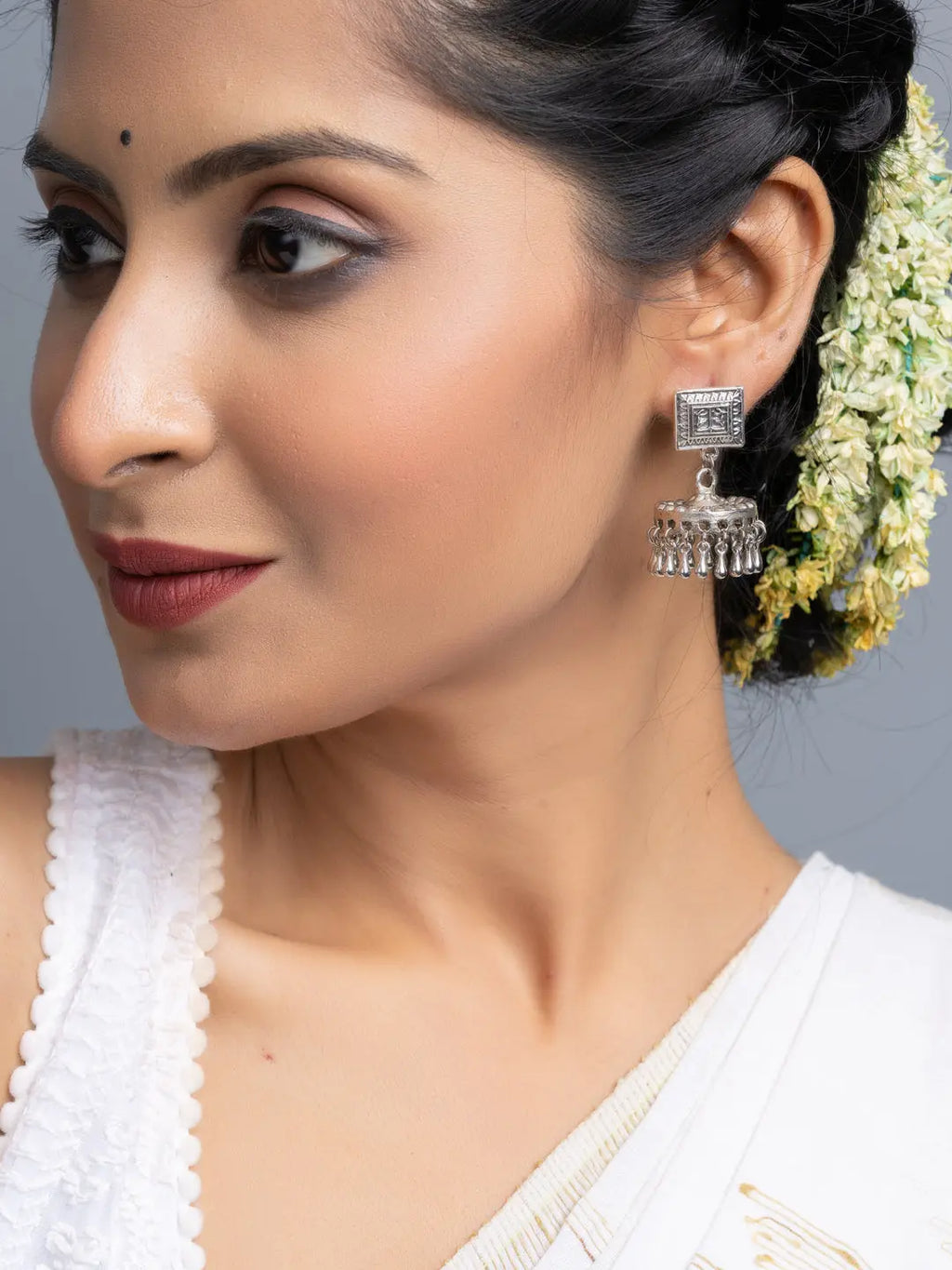Oxidised silver jhumka earrings worn by woman with traditional attire and floral hair accessory