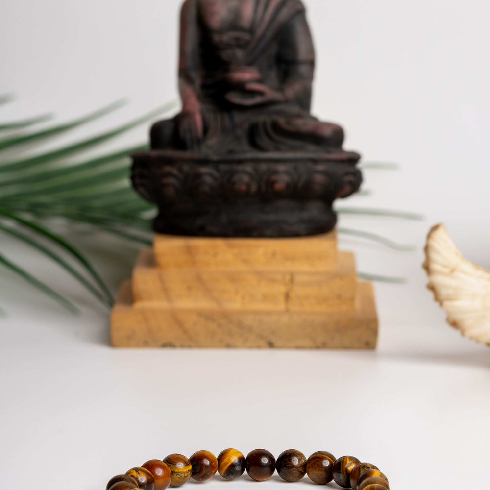 Tiger eye bracelet with polished beads, displayed in front of a serene Buddha statue