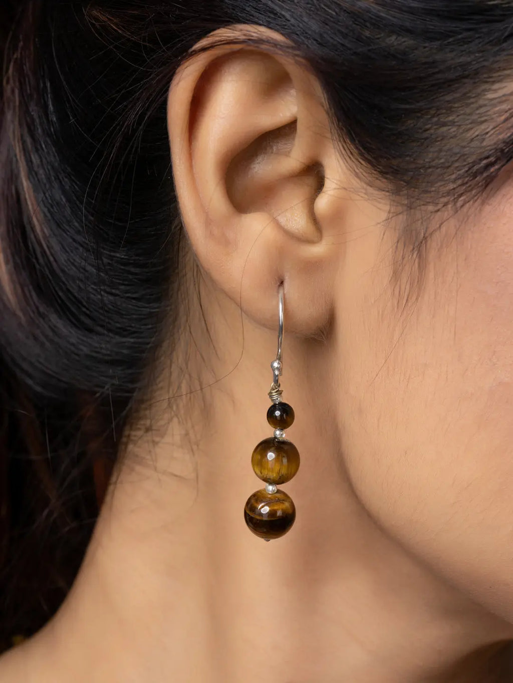 Close-up of a handmade tiger eye necklace earring with brown and golden beads on a woman's ear