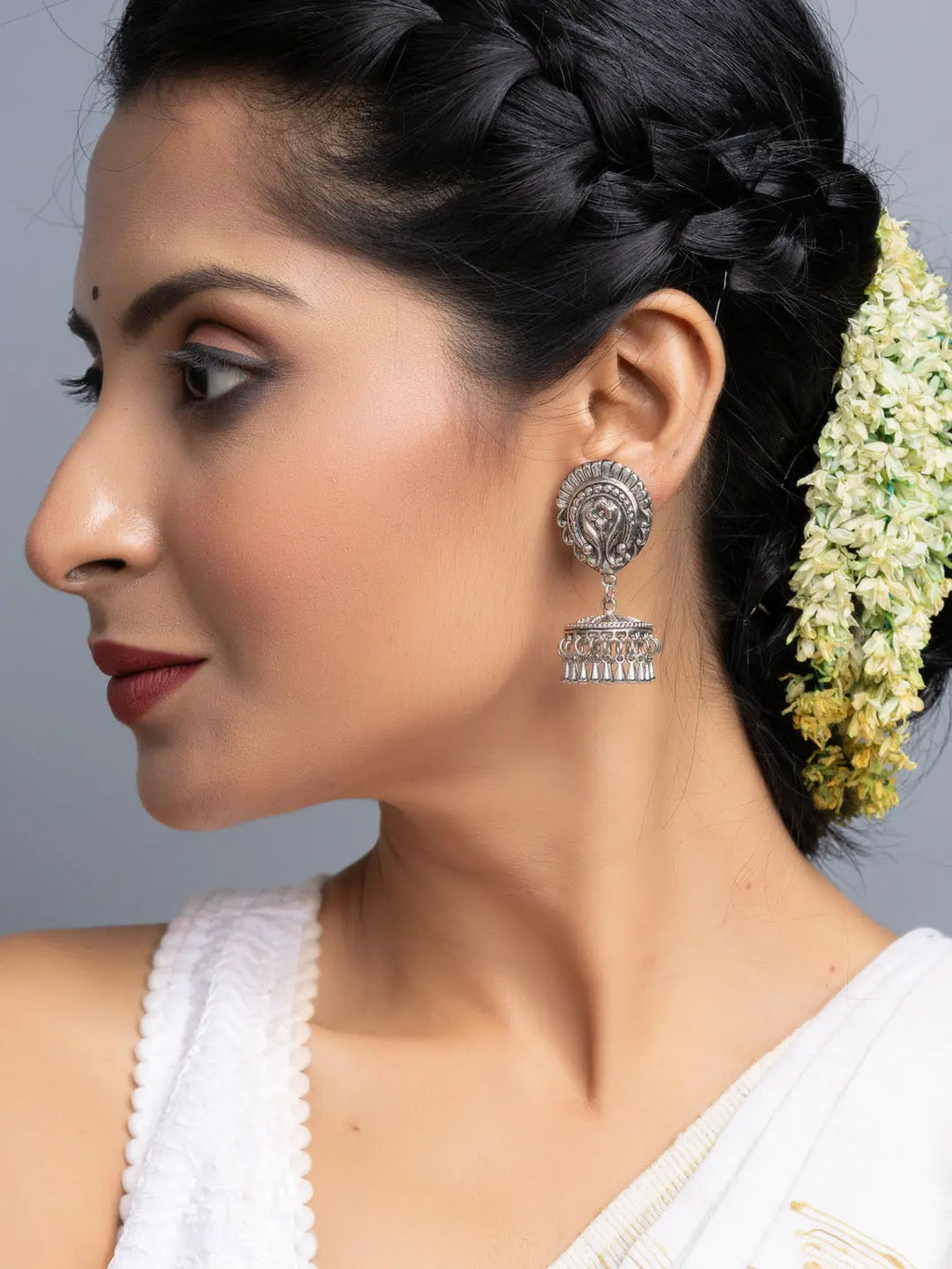 Oxidised silver jhumka earrings worn by woman with braided hair and white traditional outfit