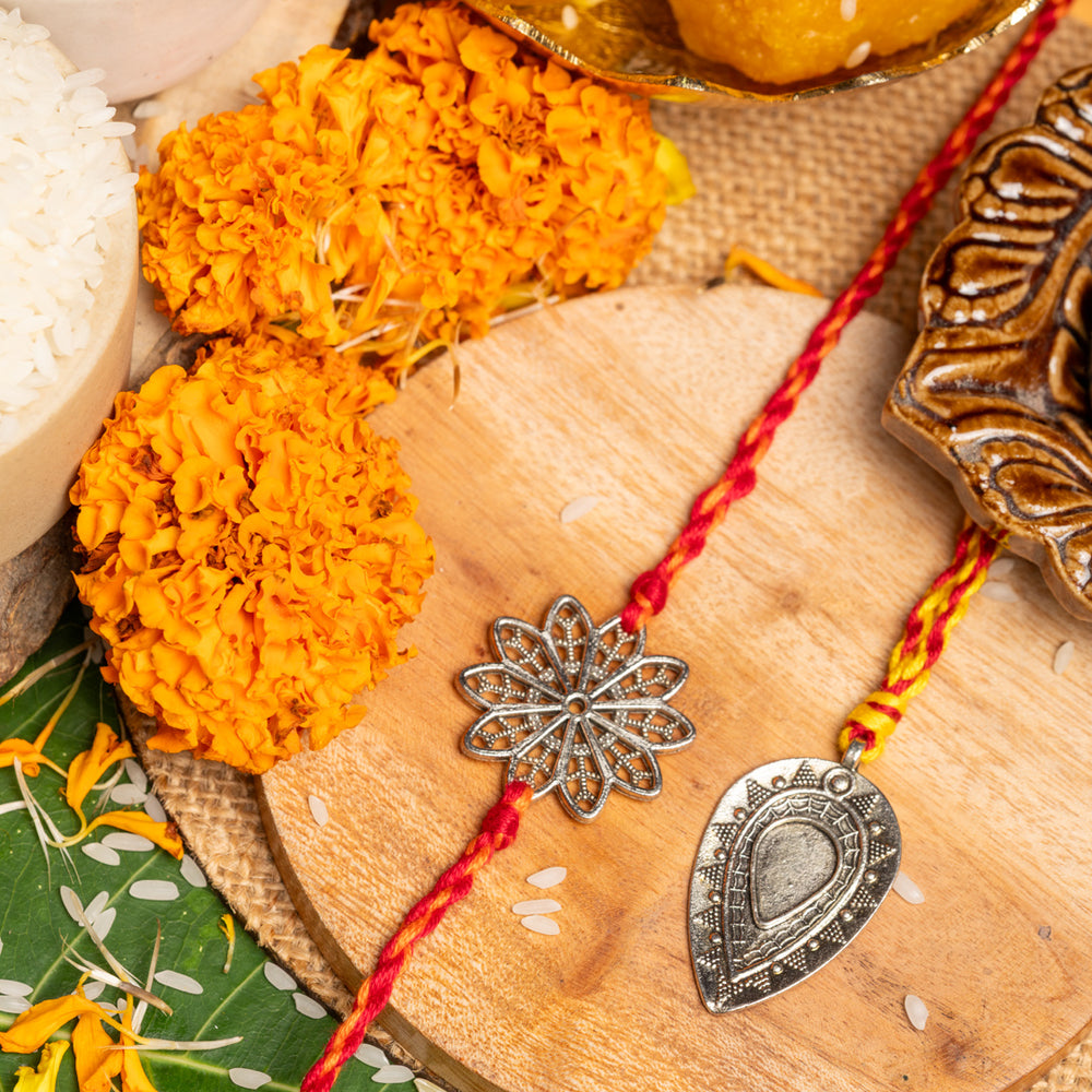 Two decorative lumba rakhi bracelets with metal charms displayed on wooden board with marigold flowers and traditional sweets