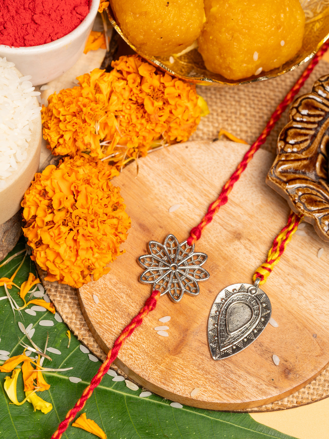 Two decorative lumba rakhi bracelets with metal charms displayed on wooden board with marigold flowers and traditional sweets