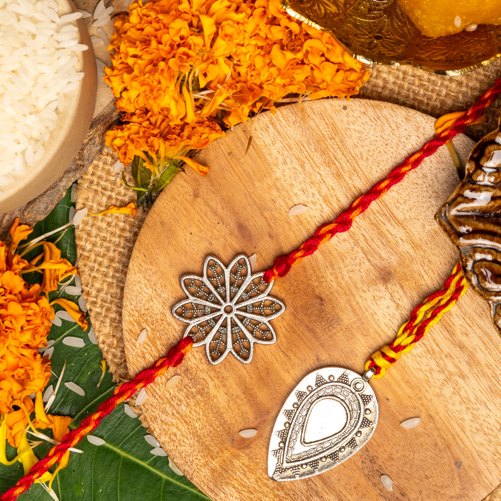 LOOK AND ADORN lumba rakhi set with silver floral and teardrop designs on wooden plate with marigold flowers and traditional items
