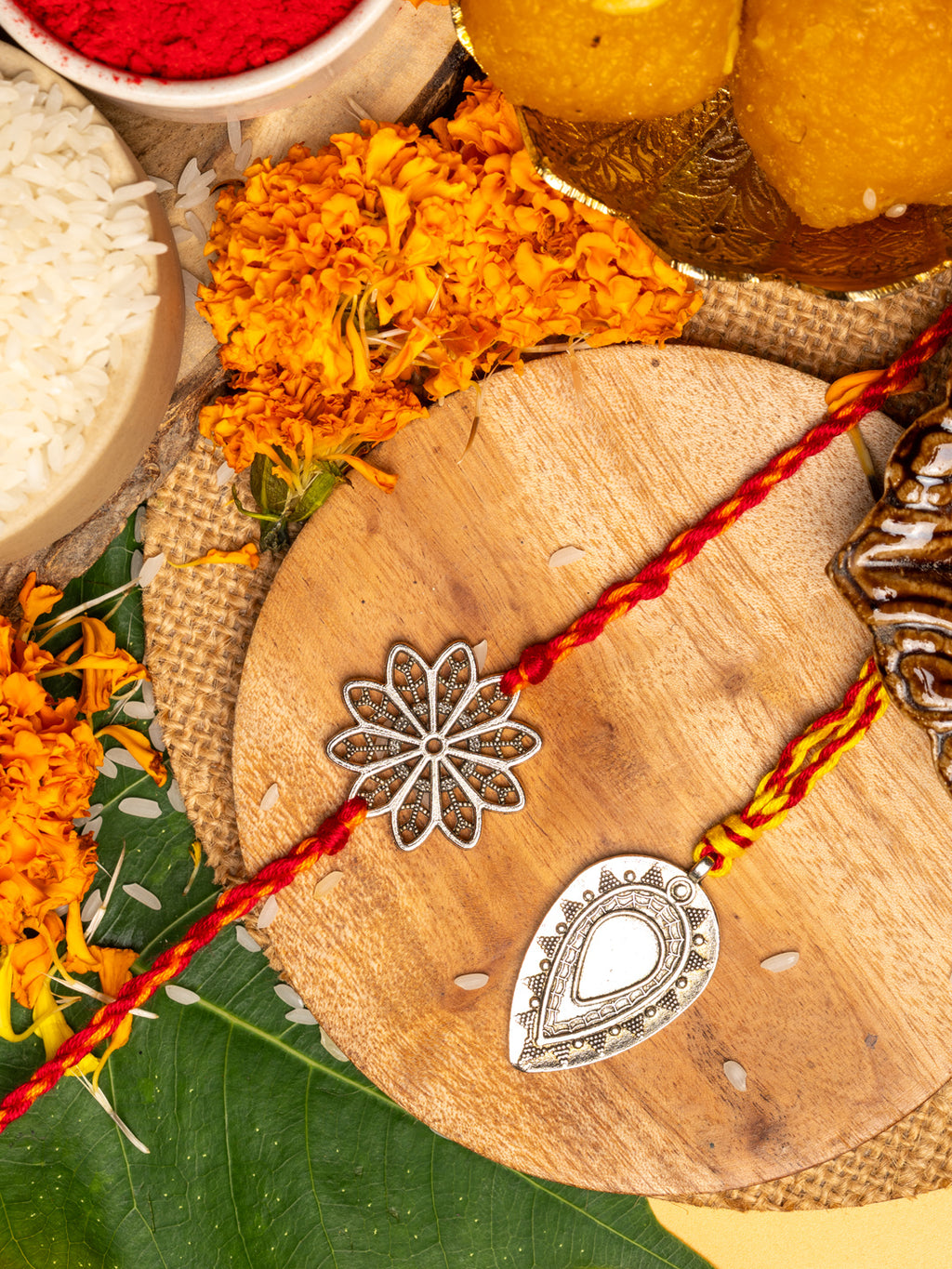 LOOK AND ADORN lumba rakhi set with silver floral and teardrop designs on wooden plate with marigold flowers and traditional items