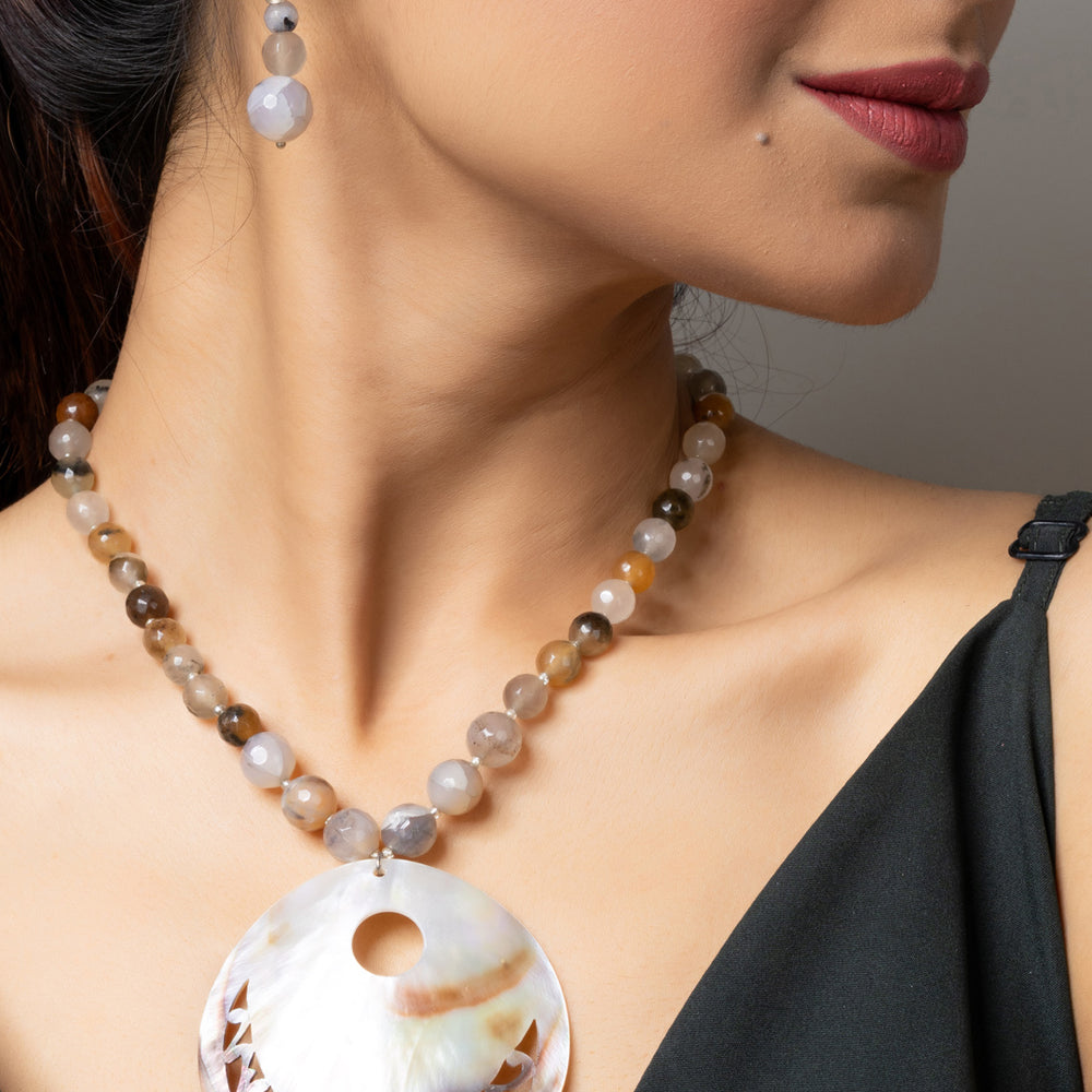 Woman wearing handmade jewelry featuring a Mother of Pearl Pendant with beaded necklace and matching earrings