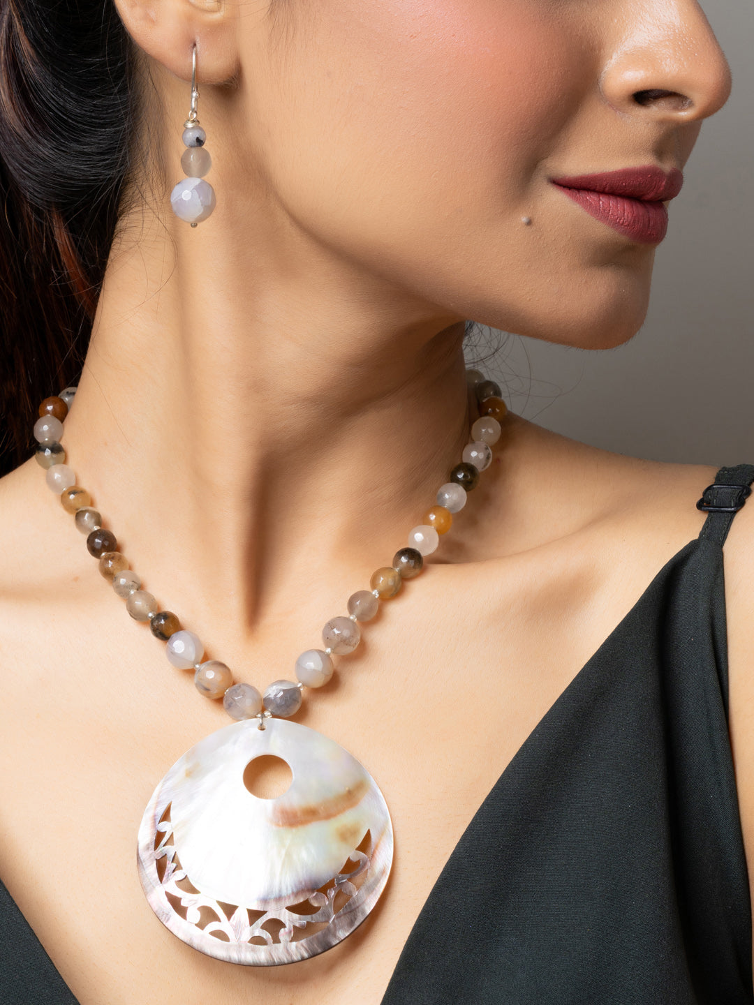 Woman wearing handmade jewelry featuring a Mother of Pearl Pendant with beaded necklace and matching earrings
