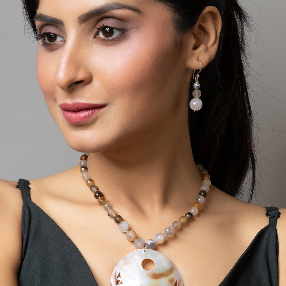 Woman wearing handmade jewelry featuring a large circular Mother of Pearl Pendant necklace and matching earrings