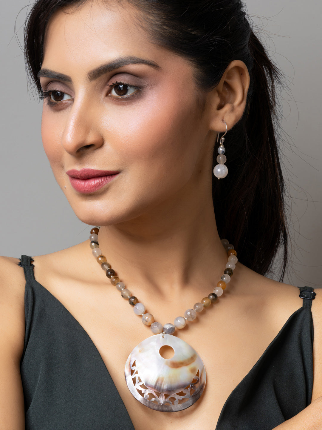Woman wearing handmade jewelry featuring a large circular Mother of Pearl Pendant necklace and matching earrings