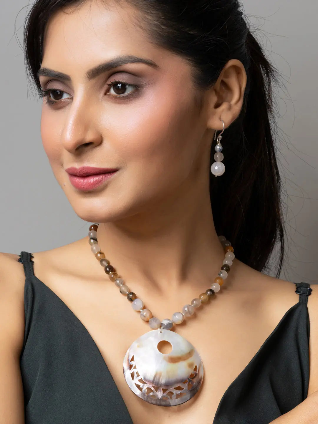 Woman wearing handmade jewelry featuring a large circular Mother of Pearl Pendant necklace and matching earrings
