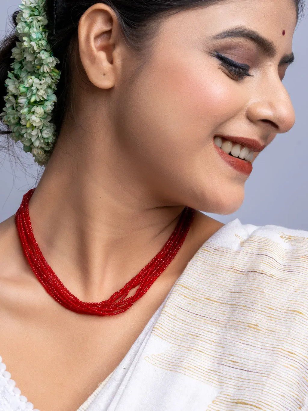 Woman wearing handmade red crystal necklace with multiple strands paired with traditional white outfit